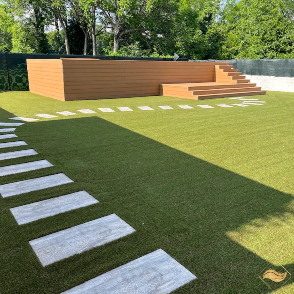 Giardino con erba sintetica e camminamento in pietra, con area relax in legno. Scopri se possibile usufruire del Bonus Verde per l'installazione del prato sintetico.