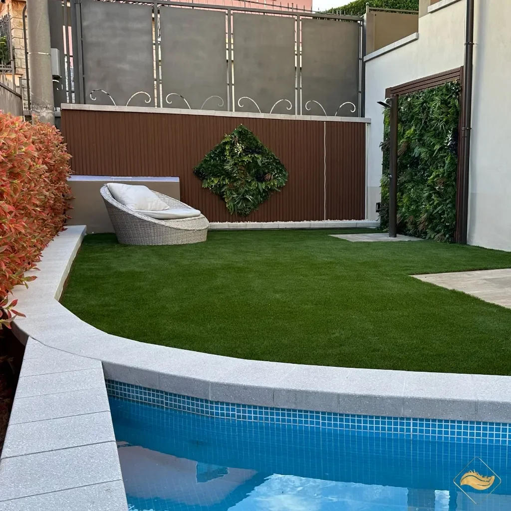 Giardino con erba sintetica intorno a una piscina, con area relax e parete verde. Ideale per piscine grazie alla resistenza all'acqua e al drenaggio rapido