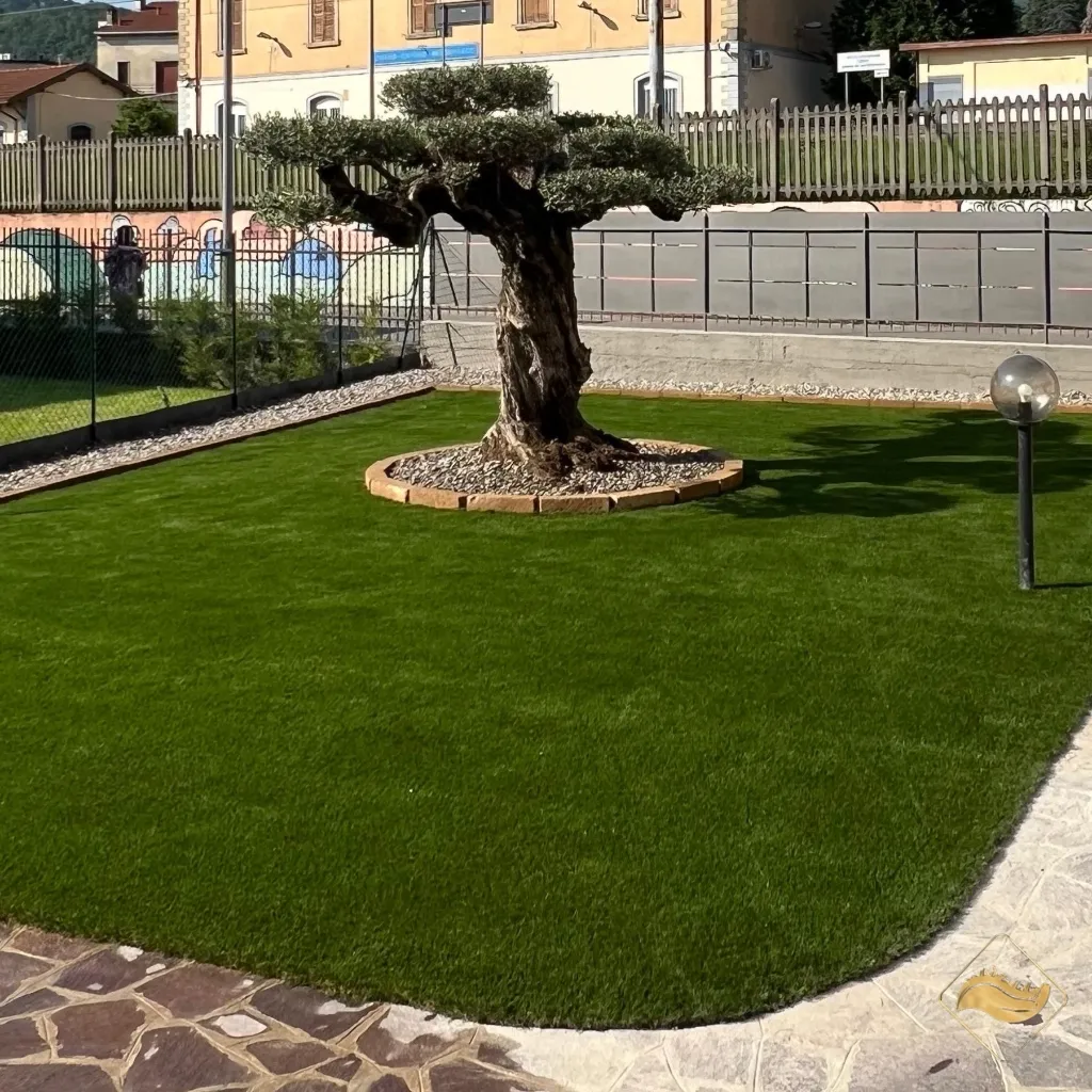 Prato sintetico realistico con ulivo secolare al centro, installazione di alta qualità per un giardino sempre verde e curato senza manutenzione.